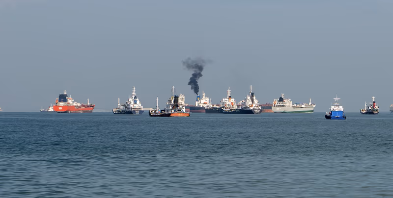 平静海面上排列的货船，其中一艘正升起黑烟