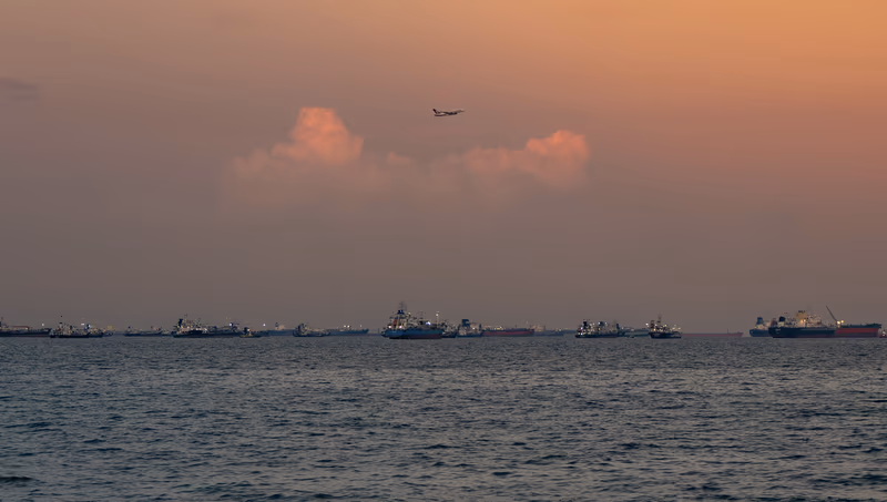 落日余晖中，海面上的货船阵列与高空飞过的A380客机