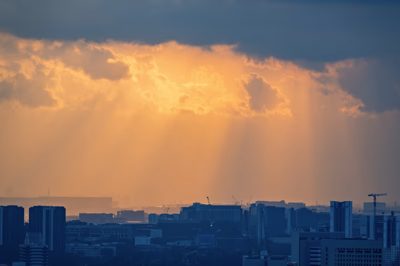 橙色的夕阳穿透云层，洒向城市天际线
