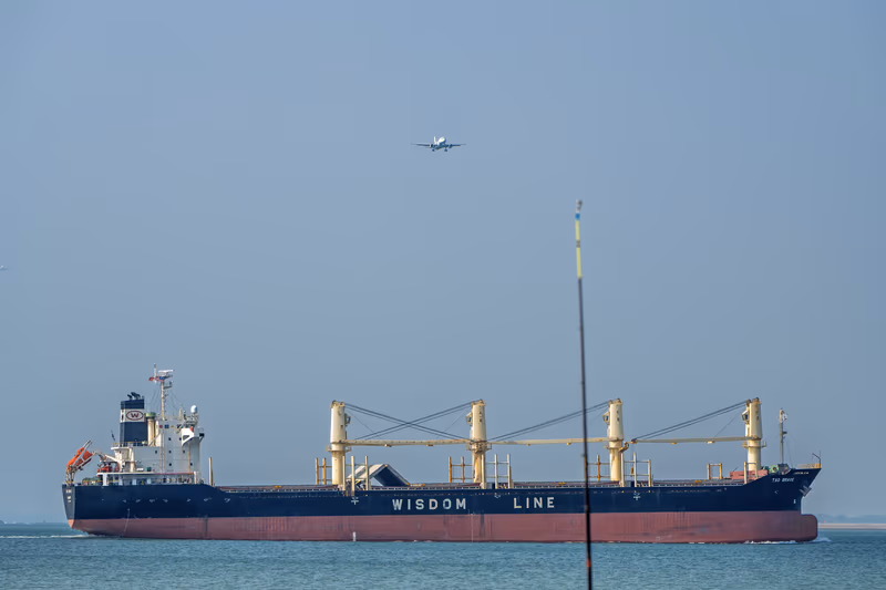 货轮驶过海面，上空一架客机正在进近